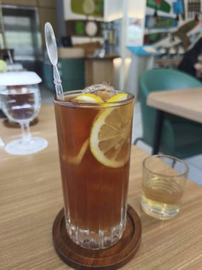 Limon dilimleri ve karıştırıcılı uzun bir bardak buzlu limon çayı, Surabaya Kafe 'deki ahşap bir masanın üzerinde duruyor..