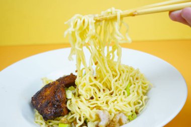 Kızarmış tavuk kanadı ve yeşil soğanla servis edilen beyaz bir tabakta, sarı arka planda servis edilen bol miktarda erişteli erişte..