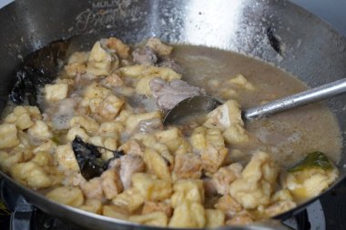 Bir metal tava lezzetli bir güveç yapar. Yanında kızarmış tofu parçaları ve metal bir kaşıkla karıştırılmış tavuk gibi görünen bir şey..