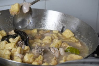 Bir metal tava lezzetli bir güveç yapar. Yanında kızarmış tofu parçaları ve metal bir kaşıkla karıştırılmış tavuk gibi görünen bir şey..