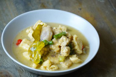 Beyaz kasede kaffir limon yaprağı ve kırmızı biberle süslenmiş hindistan cevizi sütü bazlı et parçaları ve kızarmış tofu, yeşil fasulye ile kremalı bir yahni var..