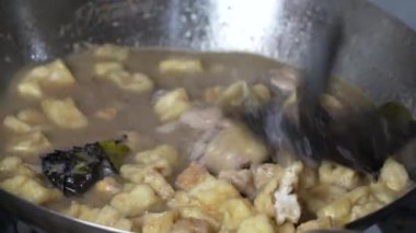 Bir metal tava lezzetli bir güveç yapar. Yanında kızarmış tofu parçaları ve metal bir kaşıkla karıştırılmış tavuk gibi görünen bir şey..