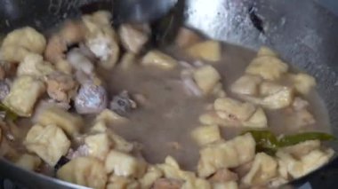 Bir metal tava lezzetli bir güveç yapar. Yanında kızarmış tofu parçaları ve metal bir kaşıkla karıştırılmış tavuk gibi görünen bir şey..