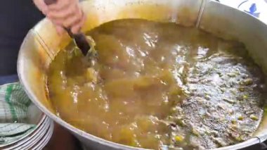 Bir insan büyük bir tencere dolusu sarı-yeşil karışımı karıştırır, geleneksel bir Endonezya soto ayam çorbası, sonra kepçeyle servis eder..