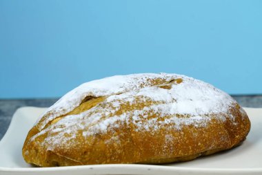 Küçük, taze fırınlanmış bir somun ekmek pudra şekerle tozlanmış, beyaz dikdörtgen bir tabakta oturuyor..