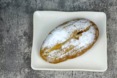 Küçük, taze fırınlanmış bir somun ekmek pudra şekerle tozlanmış, beyaz dikdörtgen bir tabakta oturuyor..