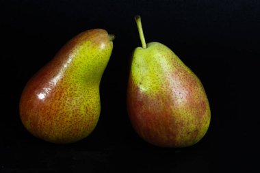 Renkli Forelle armutları koyu bir zemin üzerinde parlıyor, benekli derilerini ve taze cazibelerini vurguluyorlar..