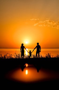 Mutlu ailenin siluetleri denizin arka planında el ele tutuşuyor, güneş, kızgın kırmızı, turuncu renkli bulutlar. Orange Sunset 'te arka plan Denizde gün batımı.