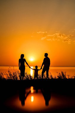 Mutlu ailenin siluetleri denizin arka planında el ele tutuşuyor, güneş, kızgın kırmızı, turuncu renkli bulutlar. Orange Sunset 'te arka plan Denizde gün batımı.