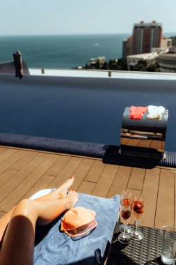 Okyanusa bakan, güneş gözlüğü, şapka ve ferahlatıcı içeceklerle okyanusa bakan havuz kenarında uzanan ve dinlendirici bir atmosfer oluşturan bir kişi..