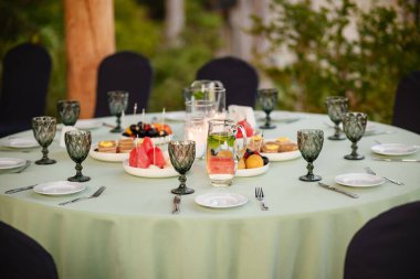 Yeşilliklerle çevrili doğal ışık altında meyveler, pastalar ve içeceklerle dışarıda toplanmak için zarif yuvarlak masa düzenlendi..