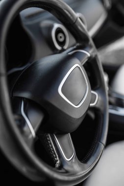 Lüks araç içinde modern araba direksiyonuna yakın çekim. Siyah deri tasarım, gösterişli gösterge paneli, yumuşak ışıklandırma, insan yok, dikey çekim, zarif otomotiv ayrıntıları..