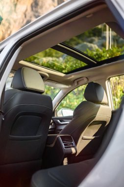 Açılır tavanlı SUV kapısından bak, siyah deri koltuklar ve başlıklar görünüyor. Manzaralı uçurumlar ve pencerelerden görülebilen yeşillikler. Gün ışığı
