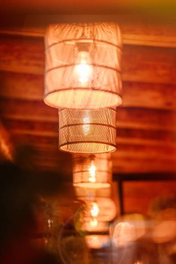 Örülmüş kolye ışıkları ahşap iç kısımda sıcacık parlıyor, yumuşak bokeh arka plan, insan yok. Zarif dekor ve samimi ayarları vurgulayan samimi ortam.