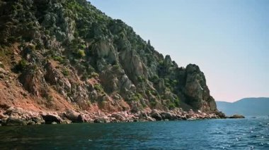 Görkemli kayalık uçurum derin mavi denizin üzerinde yükseliyor. Güneş ışığı uçurumun engebeli dokusunu aydınlatarak kayalık araziden sakin okyanusa geçişi vurgular. Doğanın saf güzelliği huzur içinde ele geçirildi..