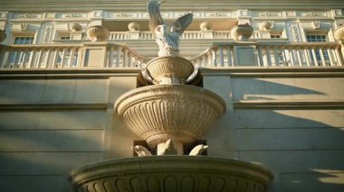 Kuğuların heykelinin zirvede olduğu süslü taş çeşme, klasik bina cephesine karşı karmaşık mimari detaylarla kurulmuş. Gün ışığı, su akışı onun zarafetini ve tarihini vurgular.