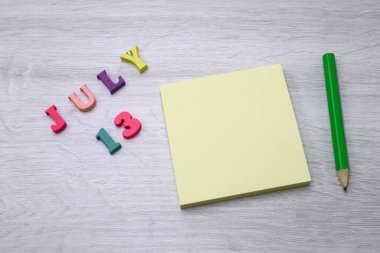 13 Temmuz - Tahta masa zemininde Blok Notlar ve Kalem içeren Günlük Renkli Takvim, metin veya tasarım için boş alan 