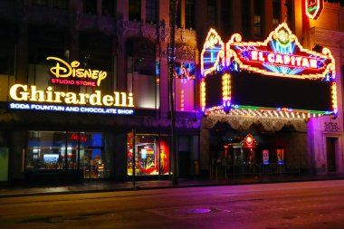 Hollywood, Los Angeles, California - July 22, 2024: The El Capitan Theatre and Disney Studio Store and Ghirardelli Soda Fountain By Night on Hollywood Boulevard Walk of Fame clipart