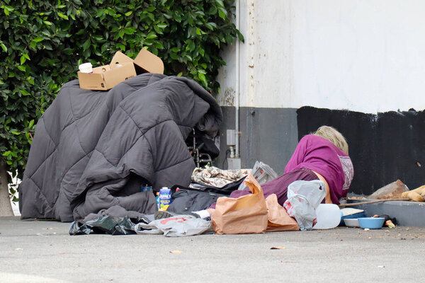 Los Angeles, California - February 27, 2025: Los Angeles, California: Homeless Person Resting on Street Surrounded by Belongings, Bowls, and Urban Debris