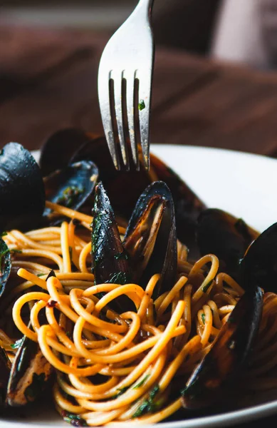 A fork over a plate of pasta with mussels, parsley, olive oil and garlic. Traditional Italian cuisine - spaghetti alle vongole. Close-up