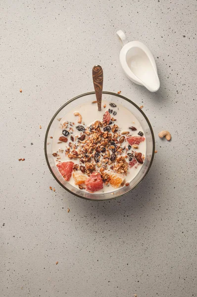 Granola (muesli) with oatmeal, milk, fruits (orange and grapefruit), cashew, pumpkin seeds and raisins in bowl on white background. Healthy breakfast concept. Perfect for stories and wallpaper