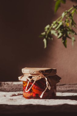Cam bir kavanoz ev yapımı güneşte kurutulmuş domates yağı. Dikey fotoğraf. İtalyan mutfağı konsepti. Arka planda yeşil domates dalı var. Kırsal biçim