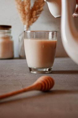 Cam bardakta sütlü bitkisel veya siyah çay. Masada şeker, bal kaşığı ve çaydanlıkla servis ediliyor. Sabah ve kahvaltı sıcak içecek konsepti. Dikey fotoğraf