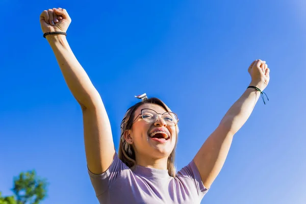 Women Day, March 8, empowered and self-confident woman. Woman expressing leadership and character. Woman happy in nature. Girl with glasses. Girl raising her hands.