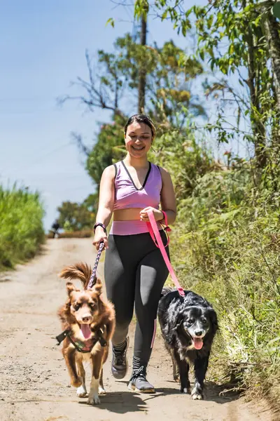 Latina woman exercising with her dogs. Woman jogging with her pets in the middle of nature. Woman walking her dogs on a sunny day. Happy dogs.