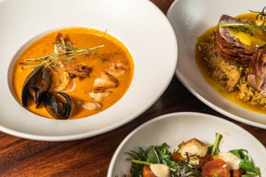 Enfes deniz ürünleri kremi, salata ve ana yemek. Otel restoranı yemeği. Ahşap masada yemekler..