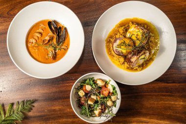 Enfes deniz ürünleri kremi, salata ve ana yemek. Otel restoranı yemeği. Ahşap masada yemekler..