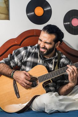 Latin bir adam odasında akustik gitar çalıyor. Ahenkli enstrüman kullanırken müzisyen şarkısı.