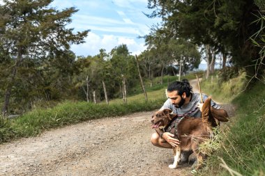 Yetişkin erkek mestizo, egzersiz sonrası köpeğini okşayıp kucaklıyor ve köpek sevgiyle gülümsüyor.