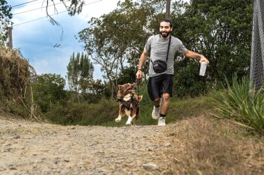 Sakallı mestizo adam neşeli köpeğiyle kırsal alanda koşuyor ve egzersiz yapıyor.