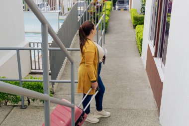 Pembe bavullu mutlu Latin kadın tatile çıkıyor. Heyecanlı kadın seyahat etmeye ve yazın tadını çıkarmaya hazır. Mutluluk ve seyahat.