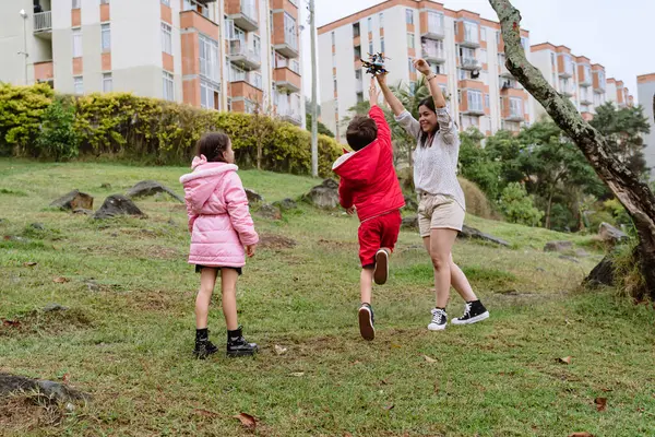 International Children Day. Latina mother having fun with her children outdoors, jumping and running. Family day with lots of fun. Concept of love and togetherness. Single mother of two young children.