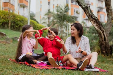 Uluslararası Çocuk Günü. Latin anne dışarıda çocuklarıyla eğleniyor. Yerde oturup, elleriyle oynuyorlar. Aile kavramı. İki küçük çocuğu olan bekar bir anne..