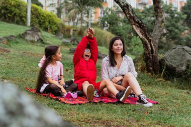 Uluslararası Çocuk Günü. Latin anne dışarıda çocuklarıyla eğleniyor. Yerde oturup, elleriyle oynuyorlar. Aile kavramı. İki küçük çocuğu olan bekar bir anne..