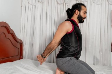 Genç adam yoga egzersizleri yapıyor ve yatak odasında esniyor. Bunu evde yap. Sağlıklı. Beyaz arkaplan.