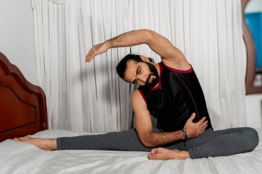 Genç adam yoga egzersizleri yapıyor ve yatak odasında esniyor. Bunu evde yap. Sağlıklı. Beyaz arkaplan.