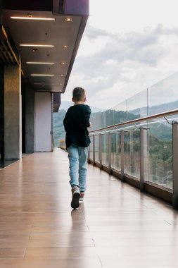 Siyah tişörtlü Latin çocuk uzun bir binanın koridorunda koşuyor, oyunlar ve eğlence. Tatiller, çocuklar günü, aile günü.  