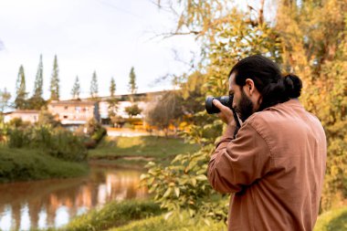 Uzun saçlı, sakallı Latin fotoğrafçı, yolculuğunun tadını çıkarıyor ve belgeliyor. Dünya fotoğrafçılık günü. Tatil ve seyahat.