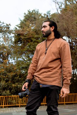 Kahverengi ceketli, uzun saçlı, sakallı Latin bir adam tatilini belgeliyor ve ülkesinin altın saatinin tadını çıkarıyor. Dünya fotoğrafçılık ve seyahat günü.