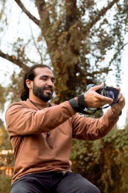 Kahverengi ceketli, uzun saçlı, sakallı Latin bir adam tatilini belgeliyor ve ülkesinin altın saatinin tadını çıkarıyor. Dünya fotoğrafçılık ve seyahat günü. 