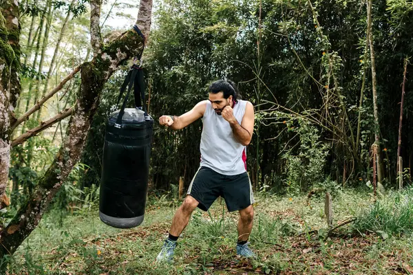 stock image Colombian man with long hair exercising with punching bag outdoors. Kick boxing, boxing, martial arts, self defense.