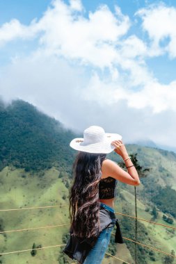 Beyaz şapkalı Latin esmer kadın, Kolombiya 'daki Cocora Vadisi' nin zirvesinde mutlu. Ailesiyle seyahat ve deneyimler..