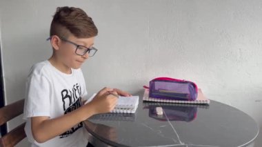 Gözlüklü Latin çocuk defterine resim çiziyor. Okula, çocukluğa. Ödev ve dersler