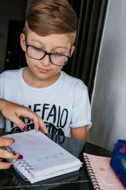 Gözlüklü Latin çocuk, annesi evde ev işleri yapıyor. Okula dönelim. Çocukluk, defterler ve eğlenceli oyunlar..