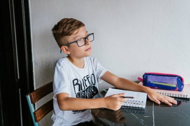 Gözlüklü Latin çocuk defterine resim çiziyor. Okula, çocukluğa. Ödev ve dersler.