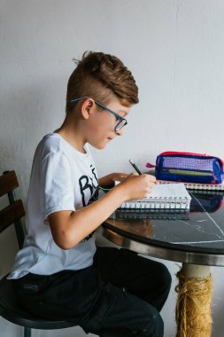 Gözlüklü Latin çocuk defterine resim çiziyor. Okula, çocukluğa. Ödev ve dersler.